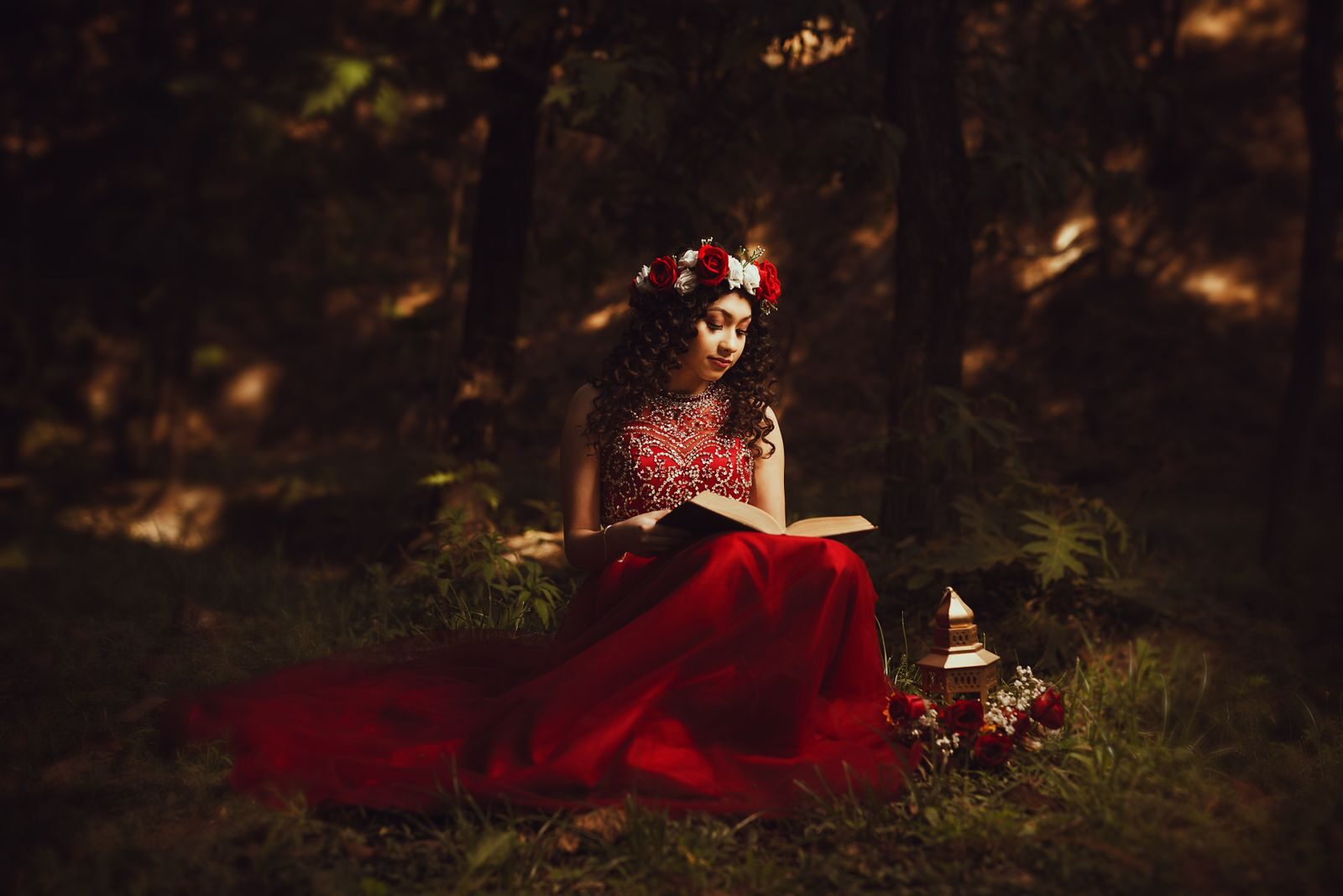 A woman in a red dress reads a book in a fairytale-like forest setting.